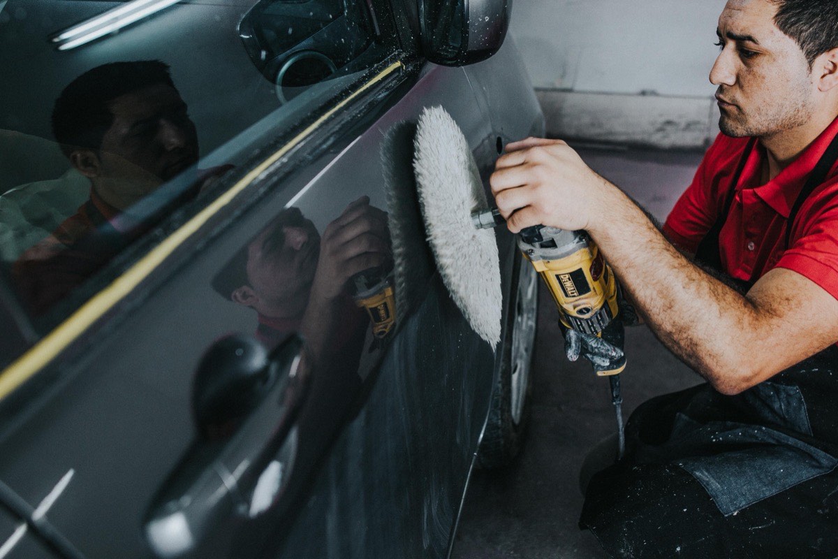 Maestro puliendo el costado de un automóvil, con el reflejo ya limpio en la pintura