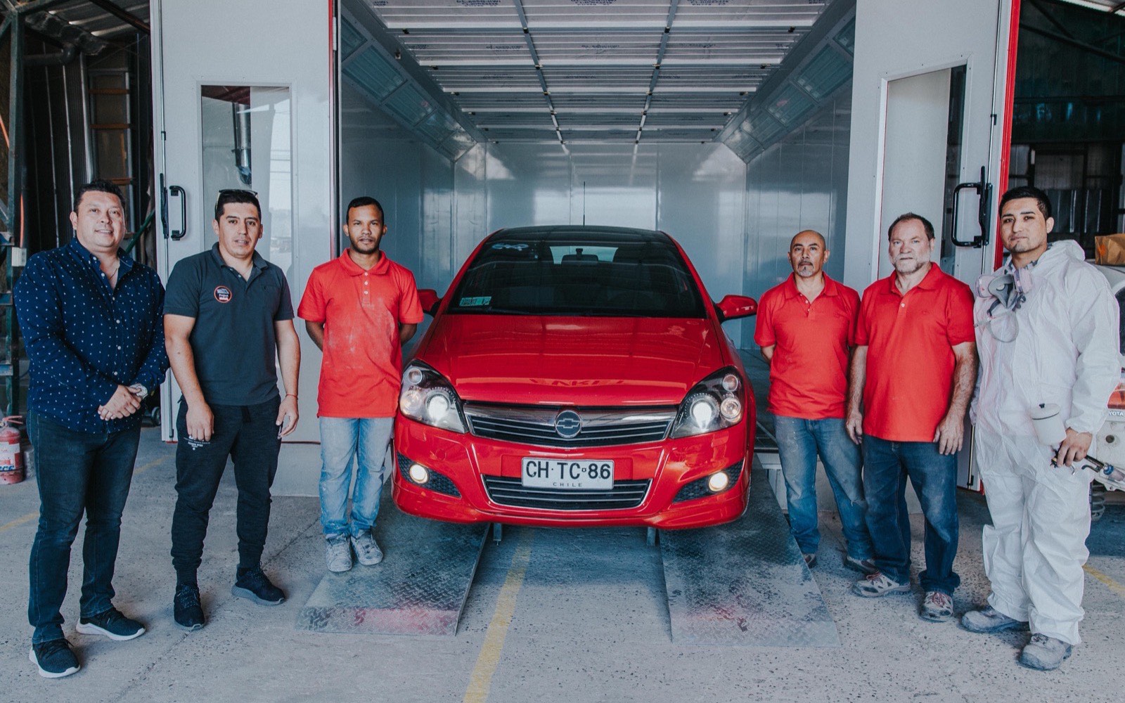 El equipo del taller reunido junto a un automóvil dentro de la cabina de pintura