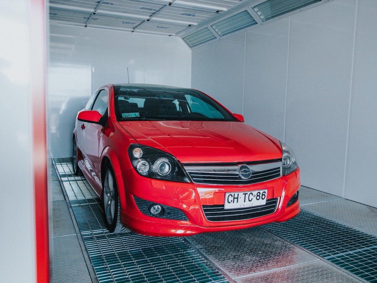 Automóvil rojo dentro de la cabina de pintura presurizada del taller